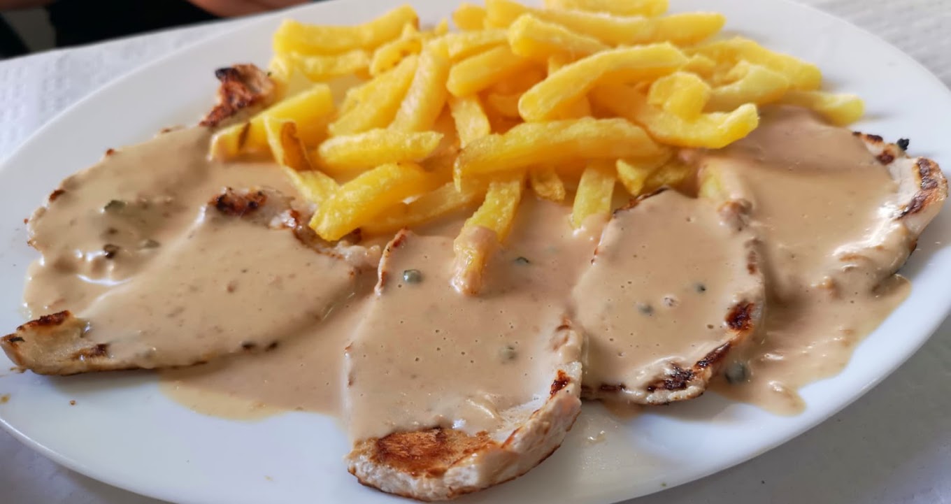 Filetes de pechuga de pollo en salsa cremosa con patatas fritas en un plato.