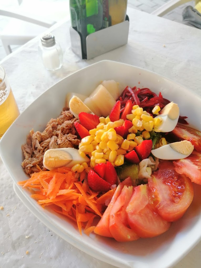 Colorida ensalada completa con ingredientes frescos y variados junto a una cerveza.
