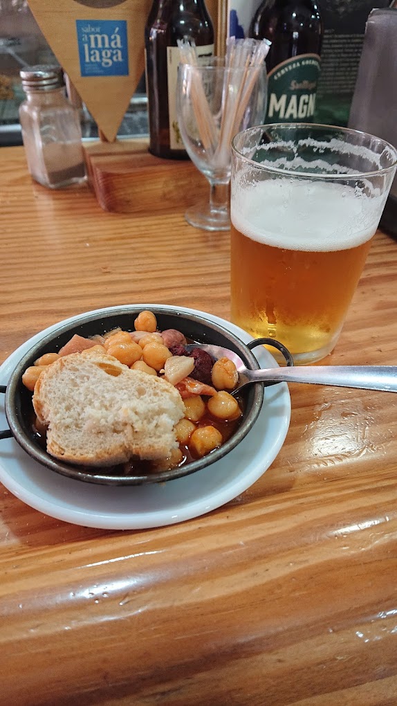 Cazuela de garbanzos estofados con un vaso de cerveza en la barra de un bar.