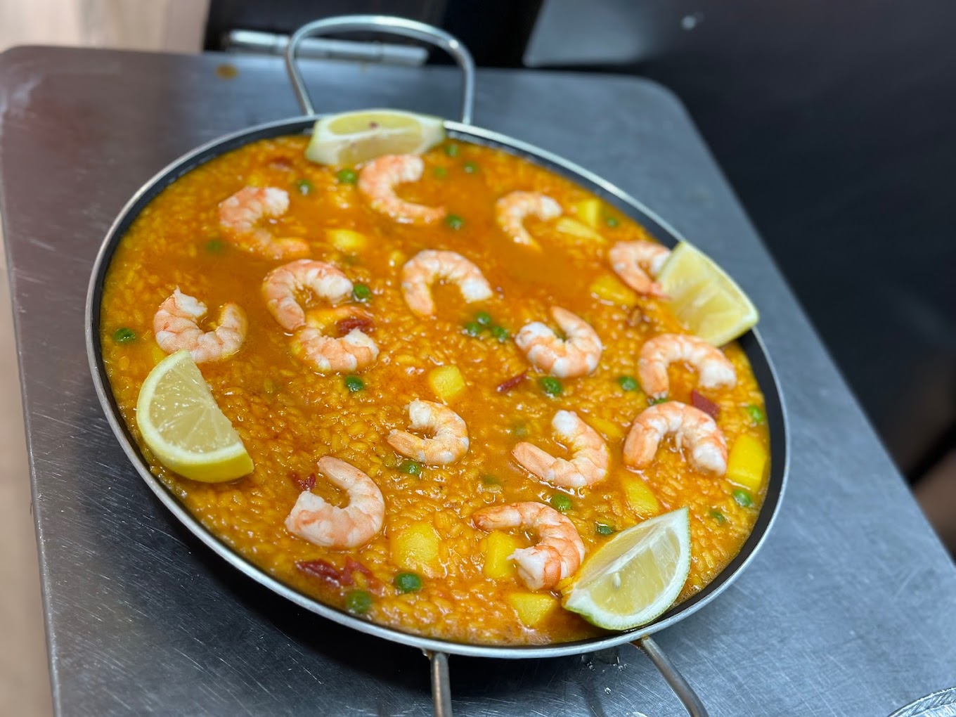 Paella vibrante con camarones y rodajas de limón servida en una paellera.